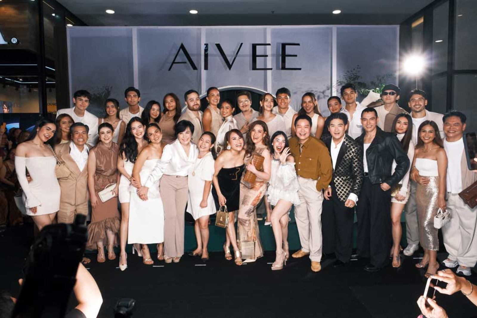 Launch guests gathered for a group photo before the AIVEE backdrop wall as photographers capture the moment